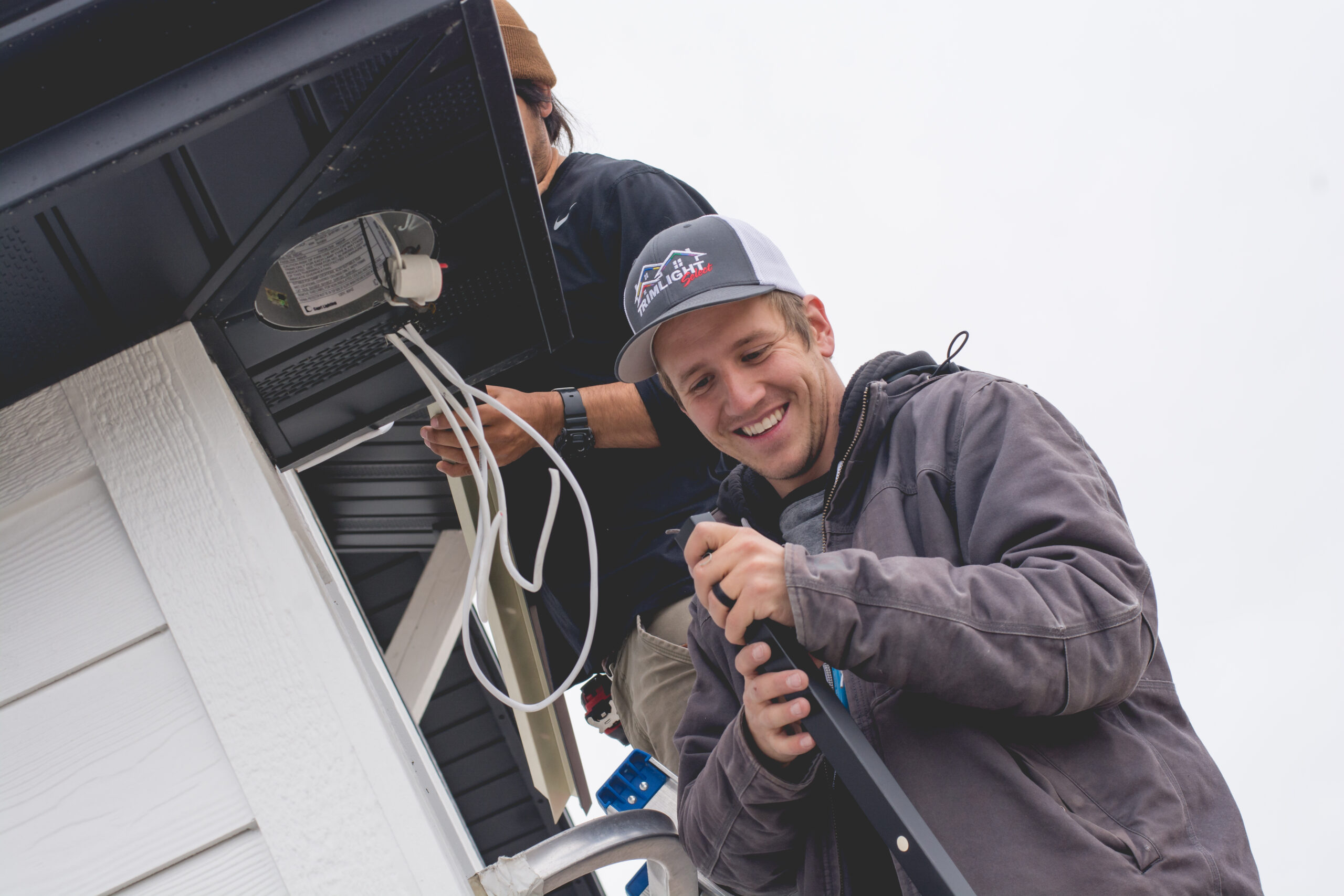 Two workers from Trimlight of Long Island installing programmable lighting system on a house.